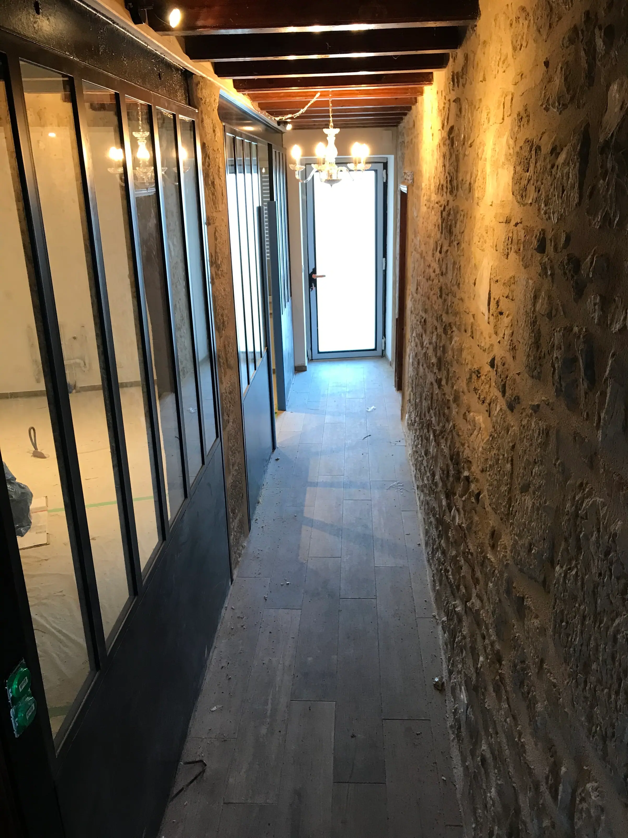 Couloir ouvert sur le séjour, mur en pierre apparente et menuiseries vitrées noires